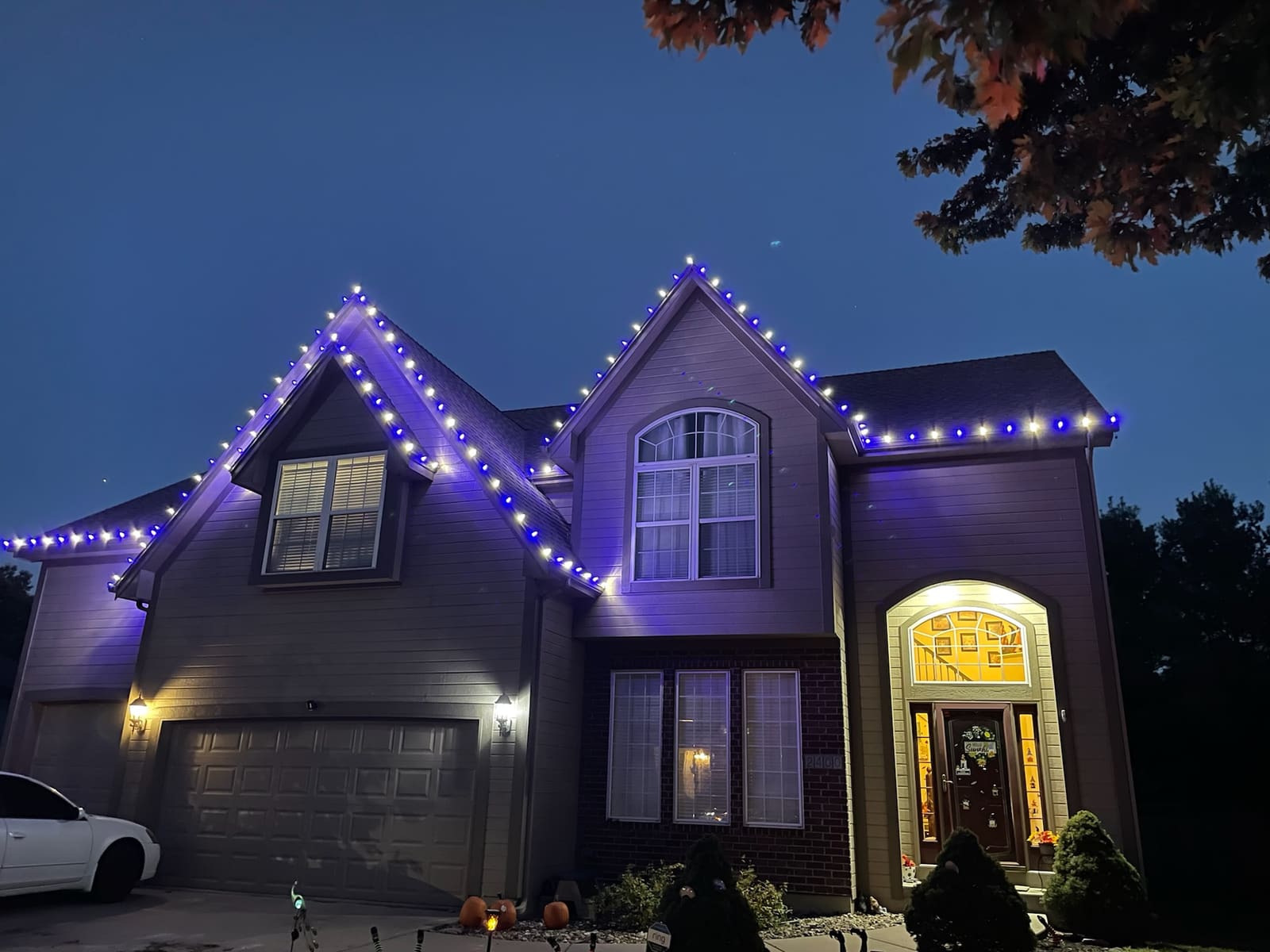 Two-story home at dusk with alternating blue and white Christmas lights along the peaks and roofline