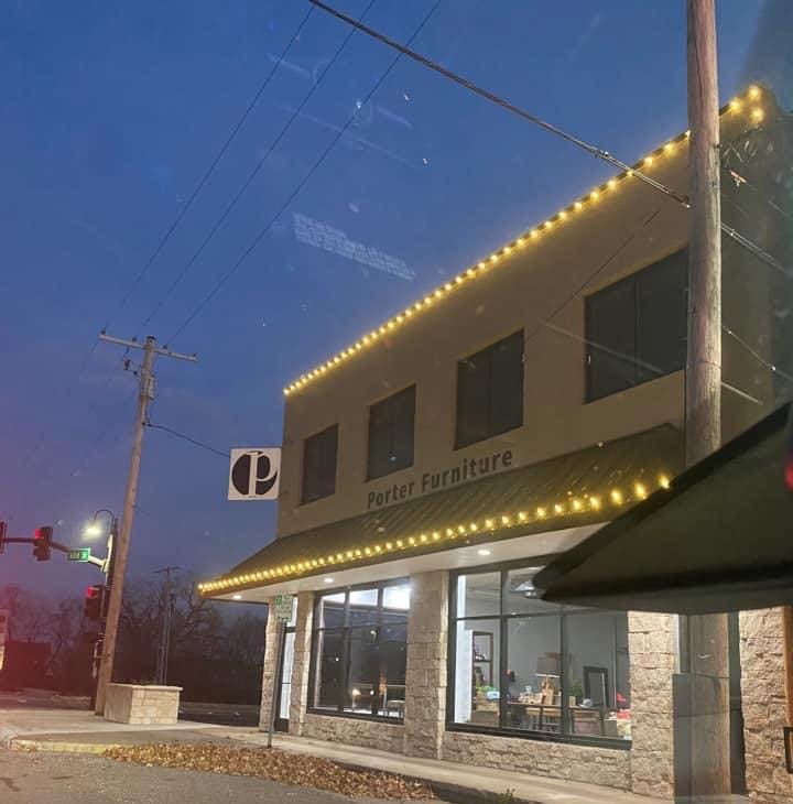Two-story retail storefront with warm white Christmas lights along the parapet roofline and front awning at dusk