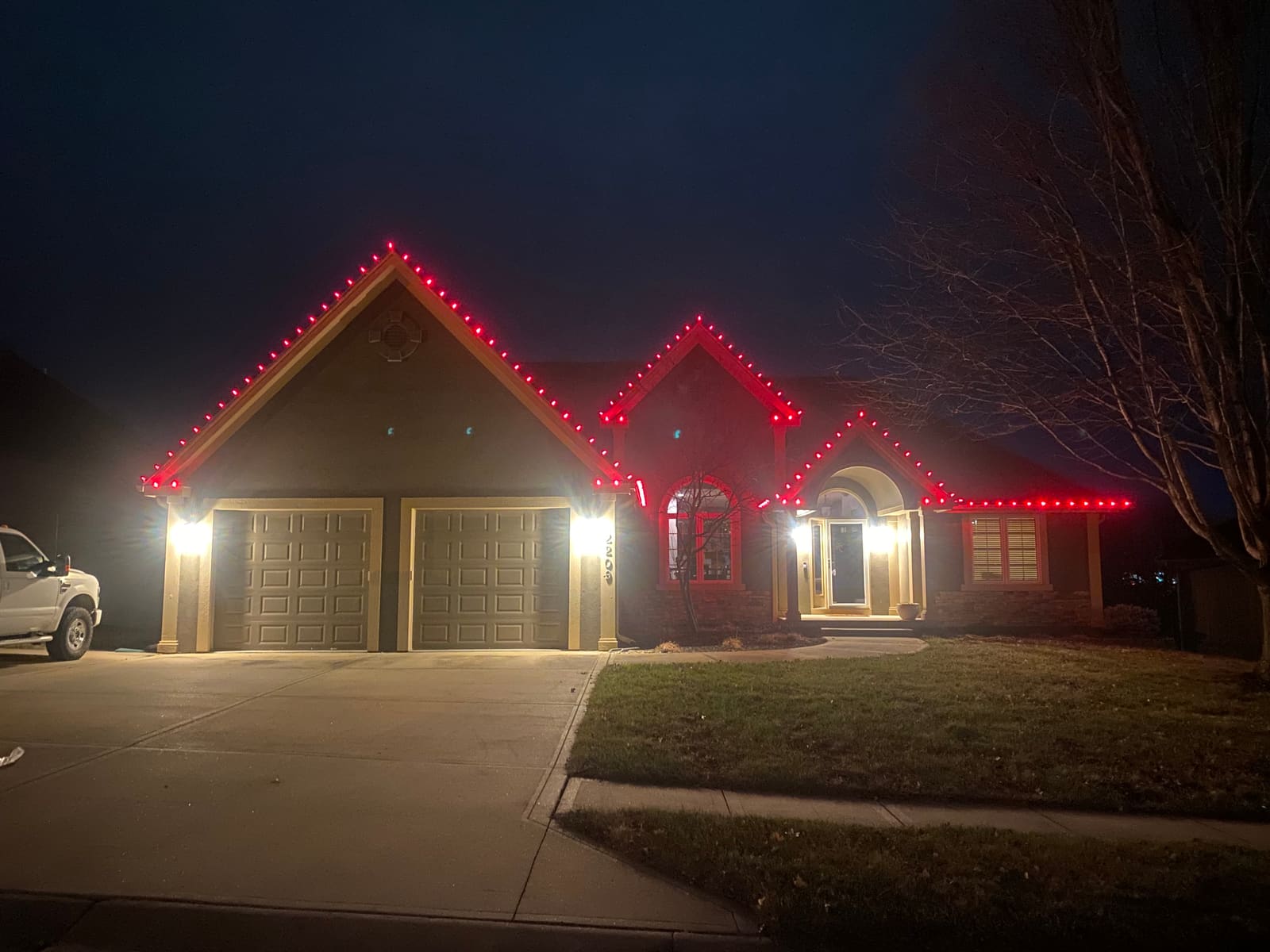 Ranch home with solid red Christmas lights outlining three front peaks and the roofline