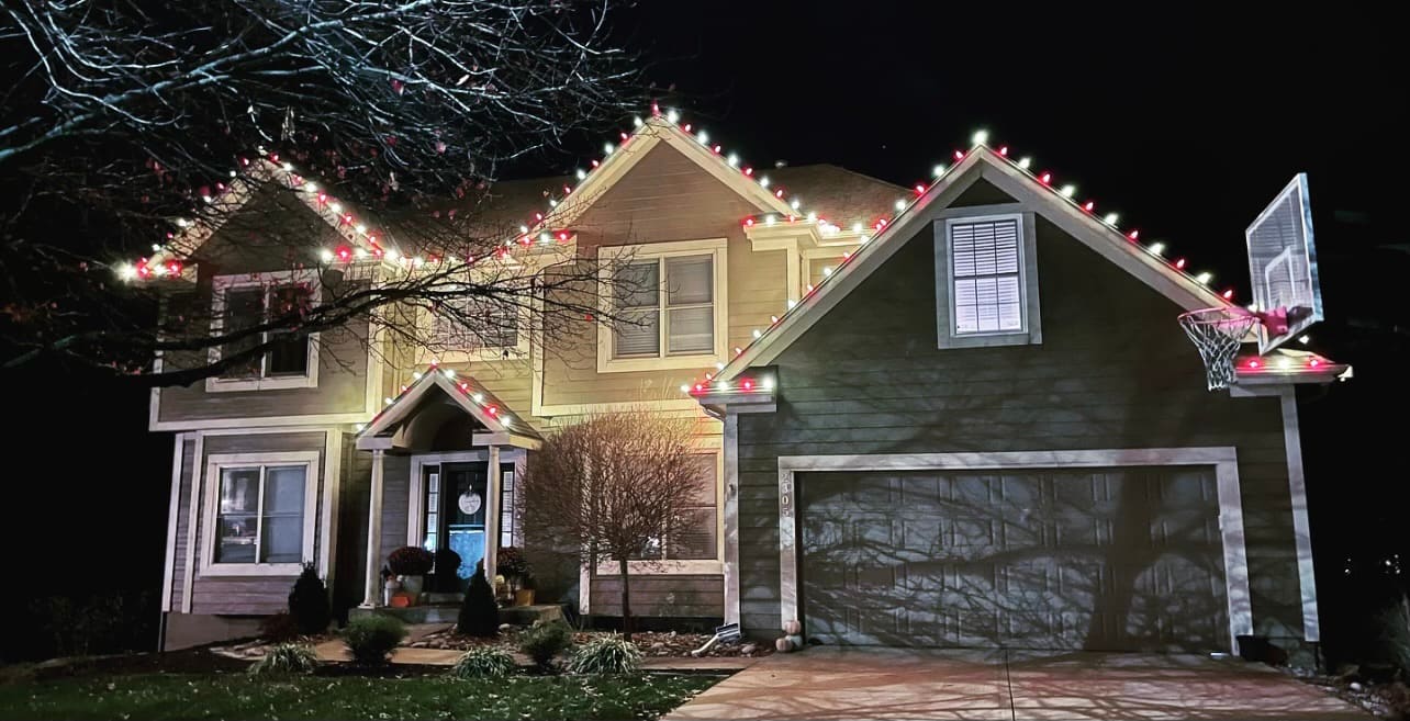 Two-story home with alternating red and white Christmas lights on the roofline and front porch gable