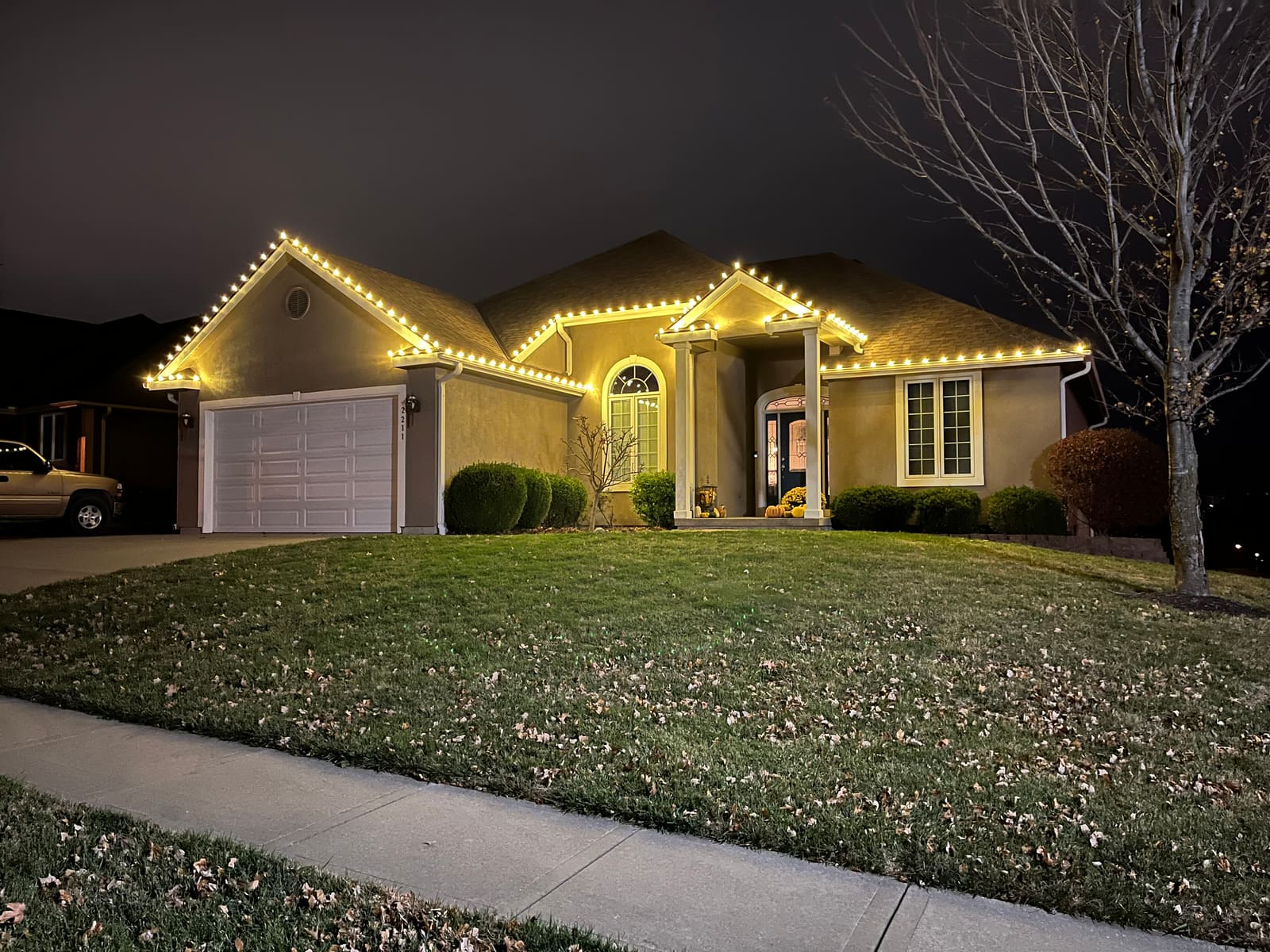 Ranch home outlined in warm white C9 Christmas lights along the roofline, peaks and front entry columns at night