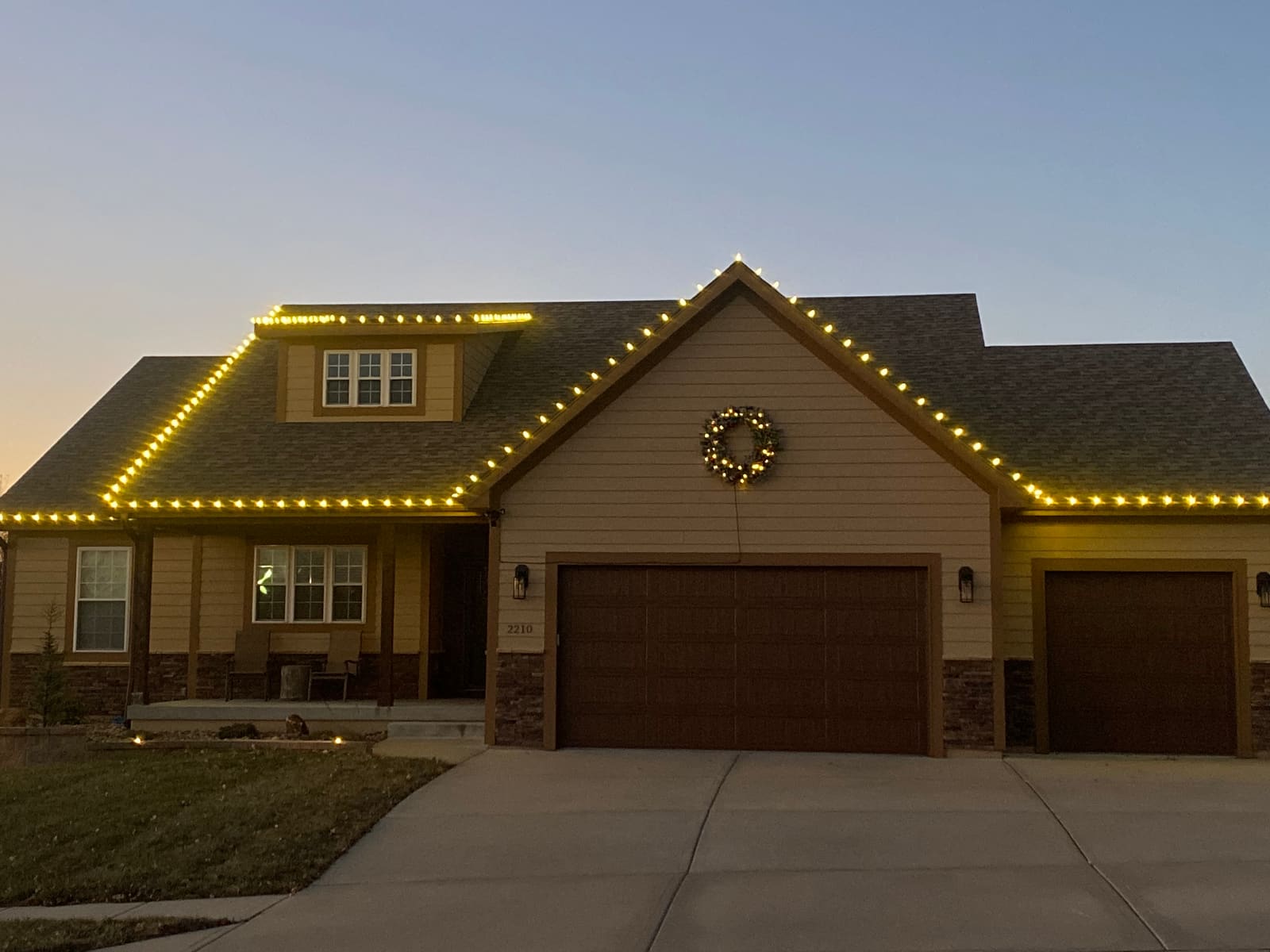 Craftsman home at dusk with warm white roofline lights, a lit dormer and a lighted wreath above the garage